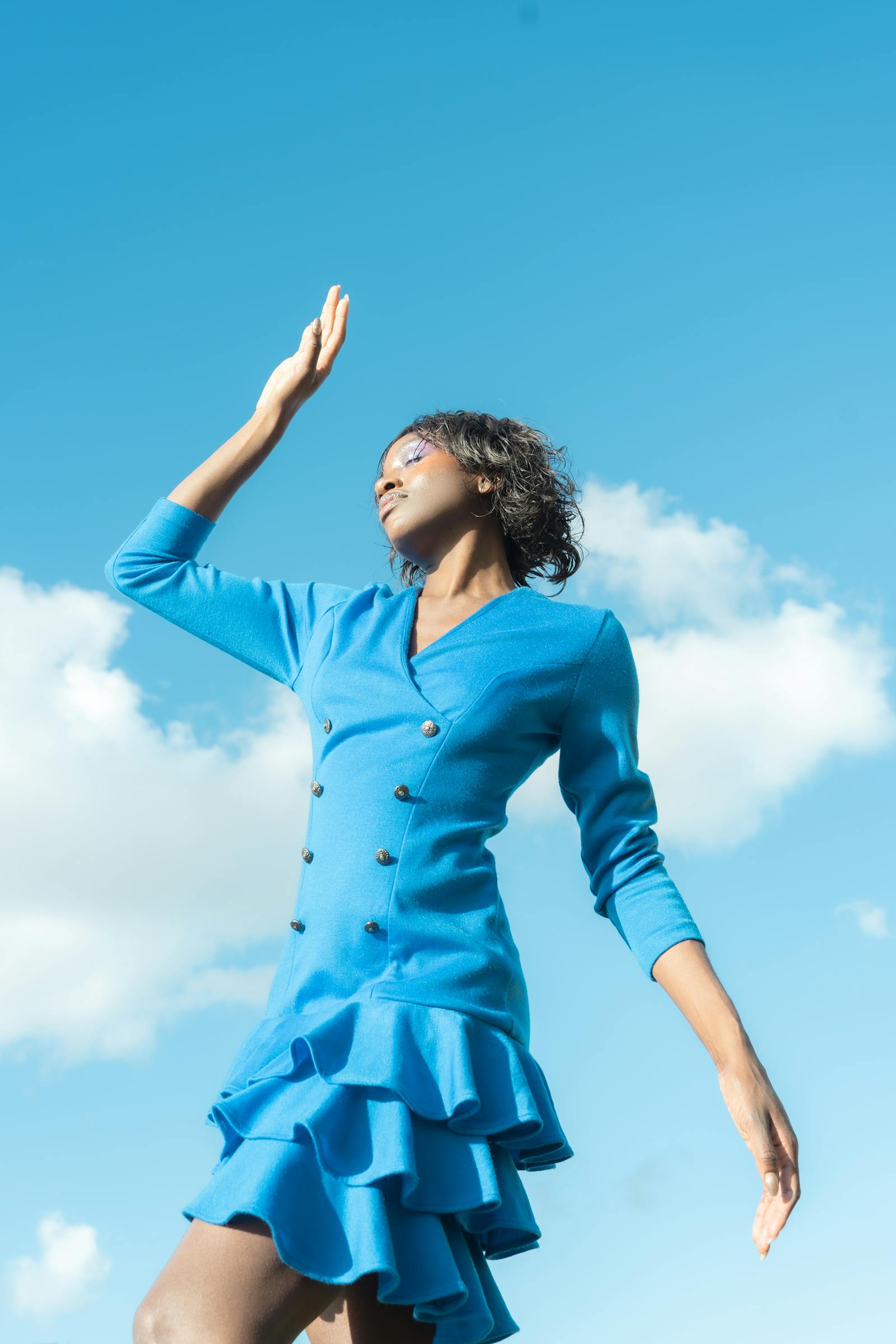 Editorial portrait of a woman in a vivid blue dress against a bright sky.